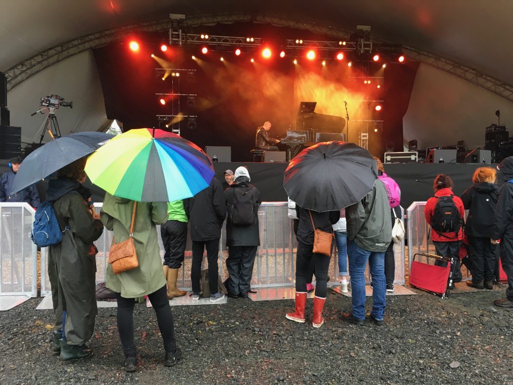 En liten publik med uppfällda paraplyer samlades framför scenen när jazzpianisten Jacob Karlzons inledde Torsjö Live. Foto: Lotta Persson