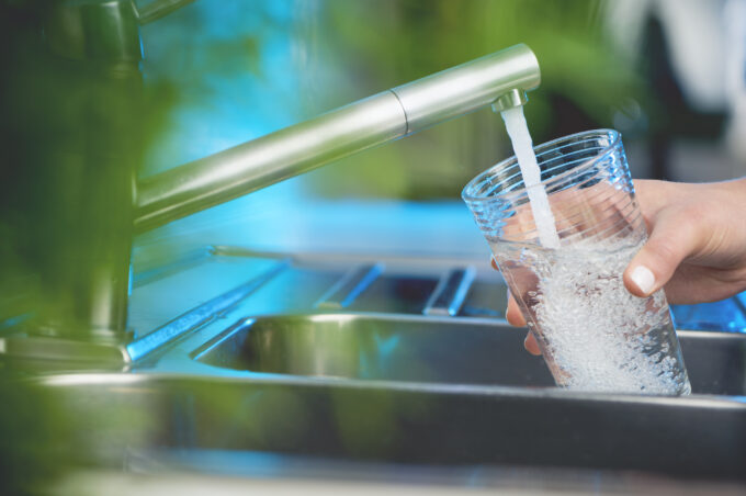 Bilden visar en hand som håller i ett glas och fyller det med vatten från en kran.