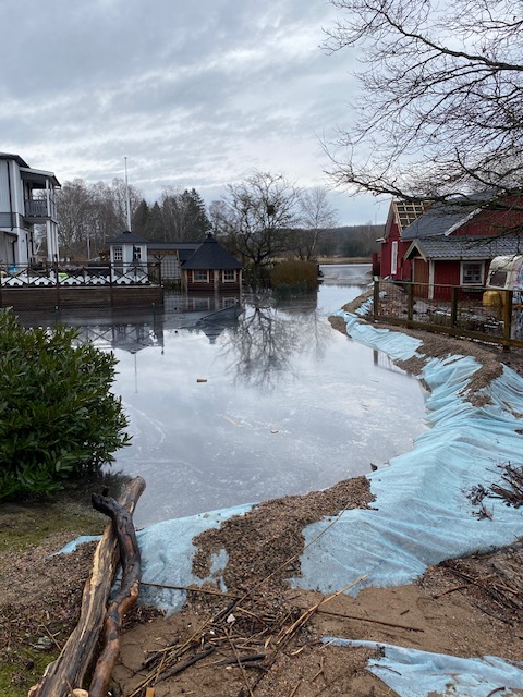 Bilden visar ett översvämmat hus med sjön vid sidan och bakom.